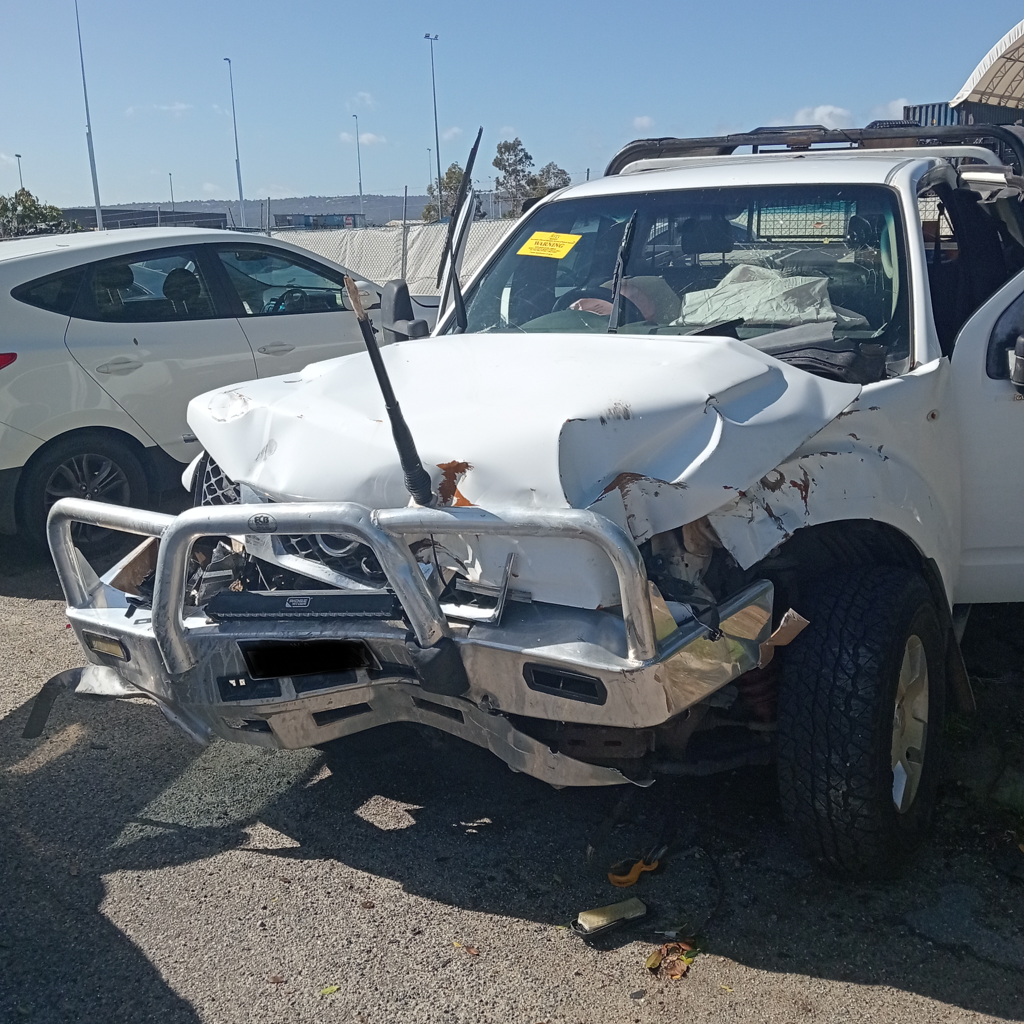Close-up of a ute's crumpled front end after a collision, parked between other vehicles